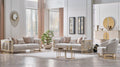 A luxury modern living room set featuring a light beige sofa, matching armchair, and a small round coffee table with gold metal legs, arranged in a bright, elegant room with beige walls, wood floors, and decorative accents.